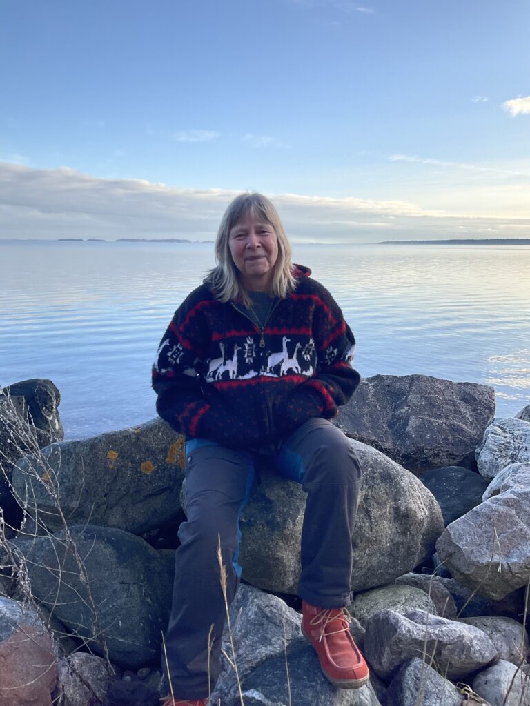 Bild på en kvinna som sitter på klippor. I bakgrunden syns öppet hav och blå himmel.