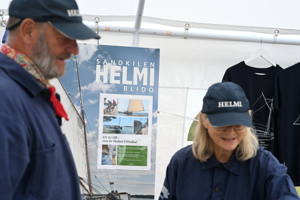 En stor affisch med texten Sadkilen Helmi, i förgrunden syns två personer i seglarkläder.